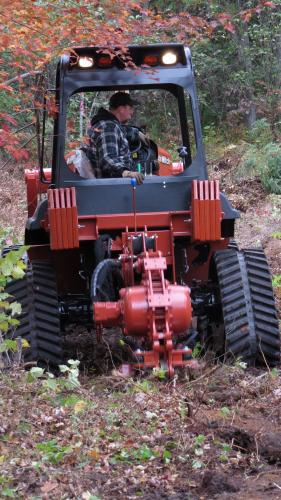 Tractor and vibratory plow operating in a forest stand.